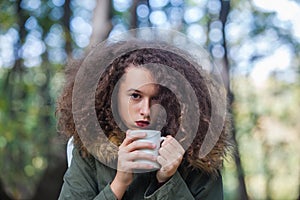 Curly hair teen girl holding mug in the park