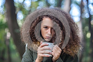 Curly hair teen girl holding mug in the park