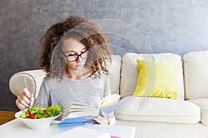 Curly hair teenage girl reading book and eating salad