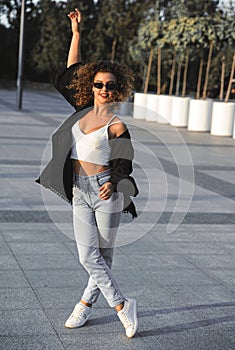 Curly hair woman in sunglasses and jacket walking in the city