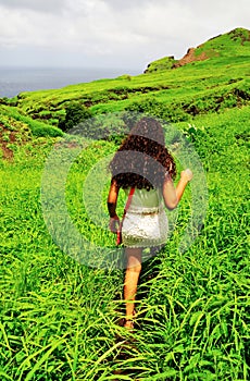 Curly hair woman walks through a lush green field