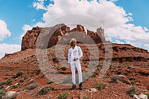 A curly haired blonde man posing around the famous Buttes of Monument Valley from Arizona, USA, wearing white linen shirt and
