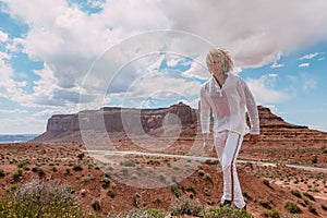 A curly haired blonde man posing around the famous Buttes of Monument Valley from Arizona, USA, wearing white linen shirt and