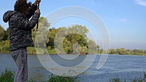 Curly-haired boy teenager fishing with a spinning rod on the lake outside the city. Male hobby fishing concept