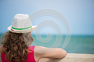 Curly haired girl at ocean coast. Rear view.