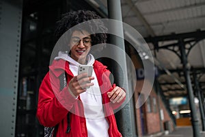 Curly-haired guy in eyeglasses with a phone in hands at the railway platform