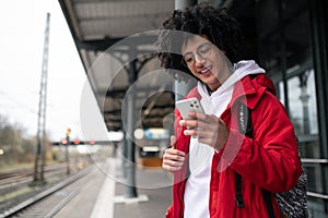 Curly-haired guy in eyeglasses with a phone in hands at the railway platform