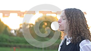 Curly-haired teenage girl inflates a big gum bubble until it bursts.