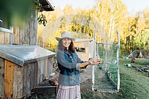 A curly-haired woman in farm clothes beams as she takes an egg from chicken coop