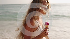 Curly-haired woman strolls along beach holding ice cream cone, savoring coastal leisure. Breezy seaside atmosphere