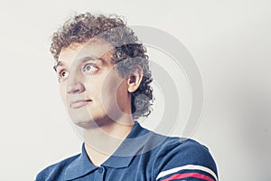 Curly haired young man on gray background with pensive expression.