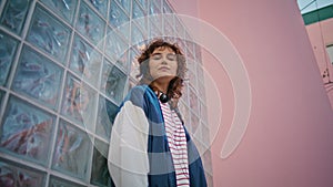 Curly hipster posing urban area looking camera close up. Woman leaning on wall