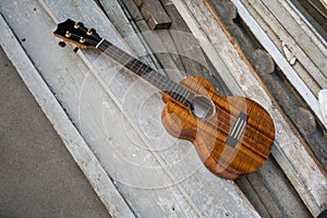 Curly koa ukulele gloss finished against wooden background.