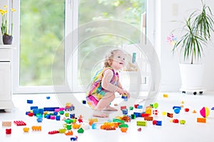Curly laughing toddler girl playing with colorful blocks