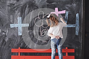 Curly little baby girl drawing with crayon color on the wall. Works of child. Cute pupil writing on chalkboard