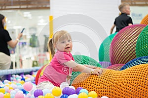 Curly little girl having fun in ball pit with colorful balls. Child playing on indoor playground. Kid jumping in ball