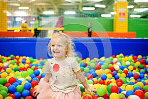 Curly little girl having fun in ball pit with colorful balls