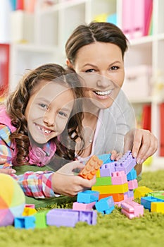 Curly little girl and her mother playing with colorful plastic blocks