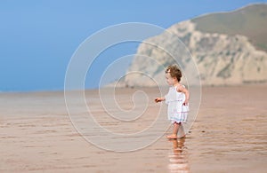 Curly little girl in a white dress on exotic beach