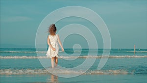 Curly little girl in white dress walking on the beach at sunset. Slow Motion. Happy Childhood, Freedom and Travel
