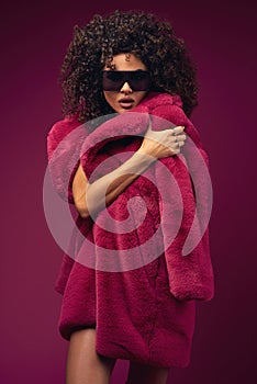 Curly model in a fur coat posing on a bright background