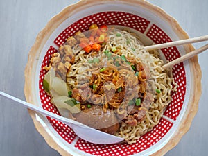 Curly noodles with minced meat, red chili slices, pickles, fried onions and egg topped in a patterned white bowl