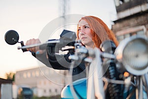 Curly red-haired woman in a black leather jacket sits on a motorcycle. Portrait of a serious girl driving a bike.