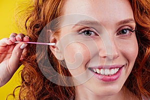Curly redhead caucasian woman use ears sticks in studio yellow background