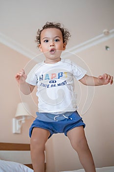 Curly toddler boy jumping and having fun on the bed
