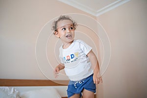 Curly toddler boy jumping and having fun on the bed