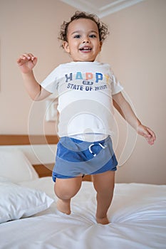 Curly toddler boy jumping and having fun on the bed