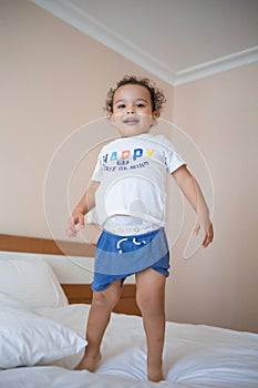 Curly toddler boy jumping and having fun on the bed