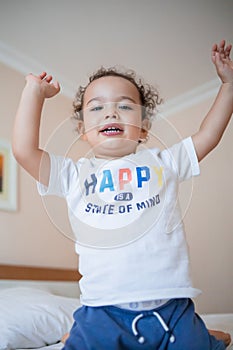 Curly toddler boy jumping and having fun on the bed