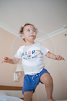 Curly toddler boy jumping and having fun on the bed