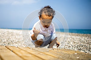 Curly toddler boy plays on the pebble beach near blue sea