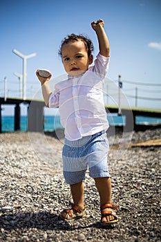 Curly toddler boy plays on the pebble beach near blue sea