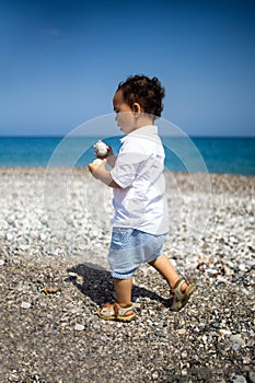 Curly toddler boy plays on the pebble beach near blue sea