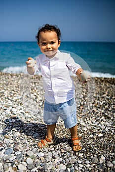 Curly toddler boy plays on the pebble beach near blue sea