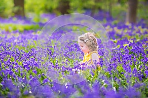 Curly toddler girl in bluebell flowers in spring forest