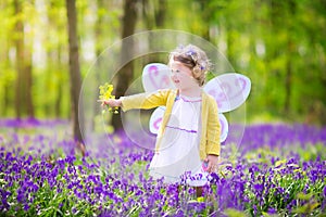 Curly toddler girl in fairy costume in bluebell forest