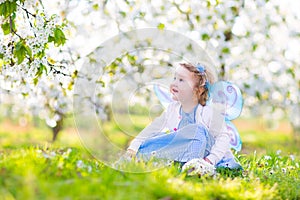 Curly toddler girl in fairy costume in fruit garden