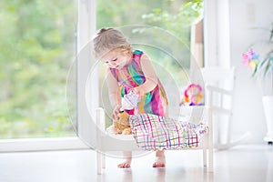 Curly toddler girl feeding her toy bear in white crib pla