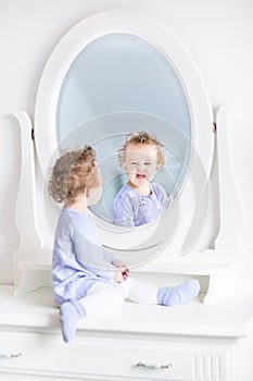 Curly toddler girl making funny faces in mirror