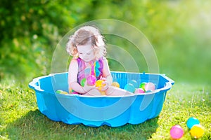 Curly toddler girl playing wil balls in the garden