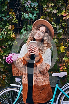 Curly woman against bicycle parked to wall covered with ivy.