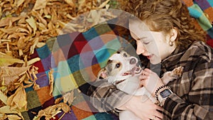 Curly woman laying on a plaid with her jack russell terrier embraced puppy in autumn park