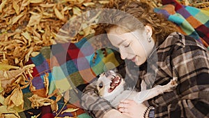 Curly woman laying on a plaid with her jack russell terrier puppy in autumn park, top view