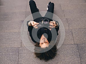 Curly woman lying down on a stone background and holding photo camera. Photographer lifestyle. Top view