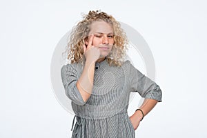 Curly woman is touching her eye to show that she has problem with eyesight.