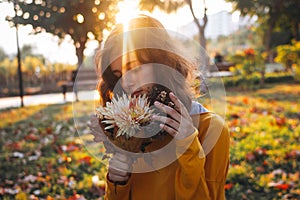 Curly young girl in yellow sweater on grass with autumn bouquet of dry leaves and flowers